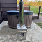 Wood-fired hot tub on a wooden platform with a scenic sunset over mountains and fields.